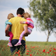 Father walking in field, holding two children on his hips.