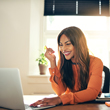 Image of business woman working on laptop with pen in hand, smiling.