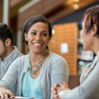 Image of business people sitting at a table together holding pens and smiling and writing on notebooks together.