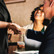 Image of two people shaking hands with a woman smiling behind.